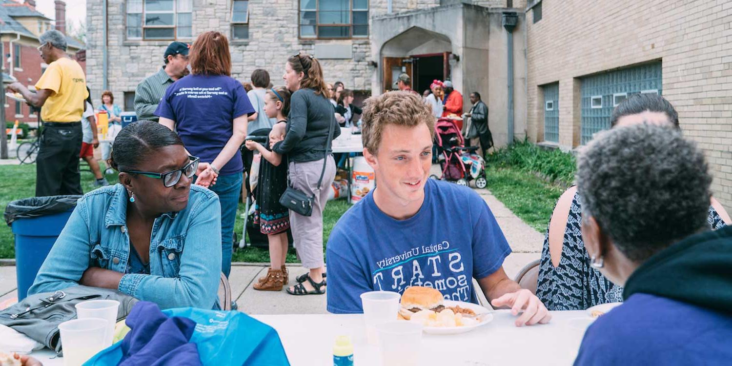 capital students eating at picnic table outside at a block party